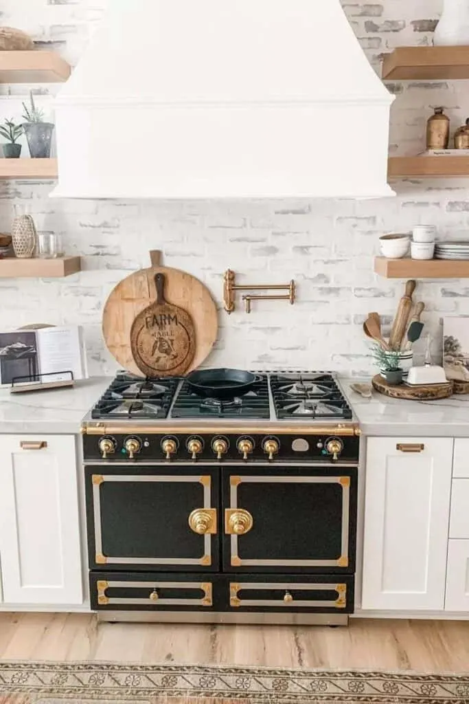 White cabinets and a brick backsplash with a white wash treatment and a black old world stove/oven with gold accents.