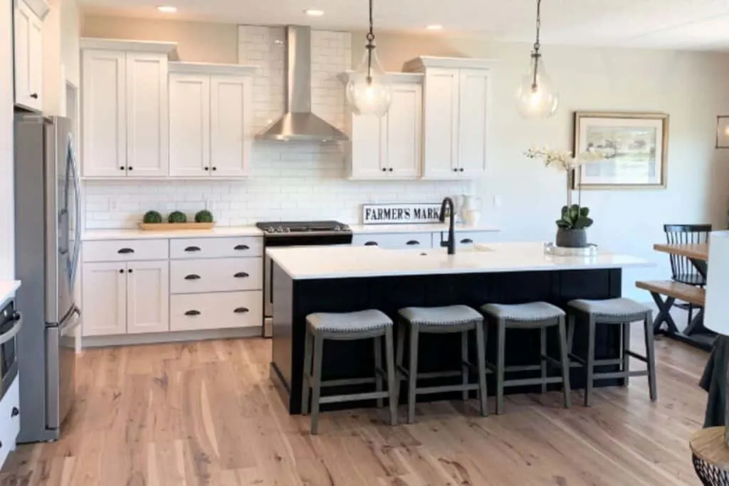 A white kitchen with a black island and light hardwood floors.