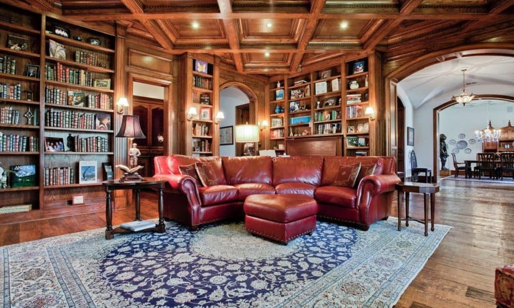 A family room with wood floors and an area rug, all wood shelving and a wood coffered ceiling.