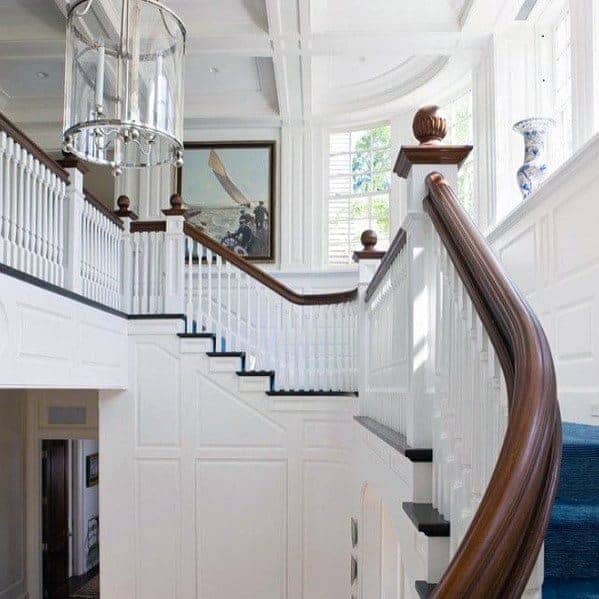 A grand staircase in an entryway with molding on the walls, blue carpet on the stairs and a white coffered ceiling that has a curve to it.