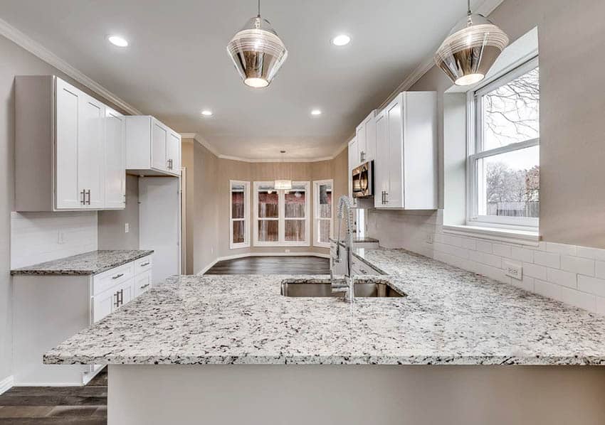 White cabinets with white granite countertops that have flecks of brown and gray in it.