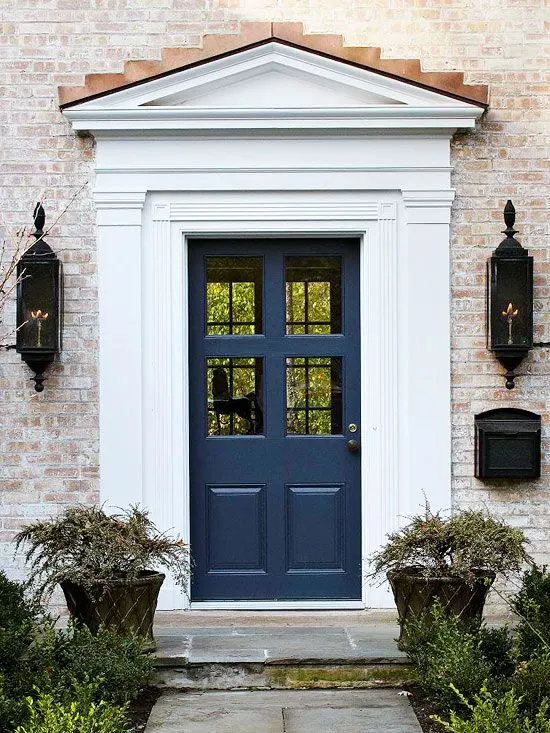 A faded brick house with a navy blue door and white trim with black gas lanterns flanking the door.