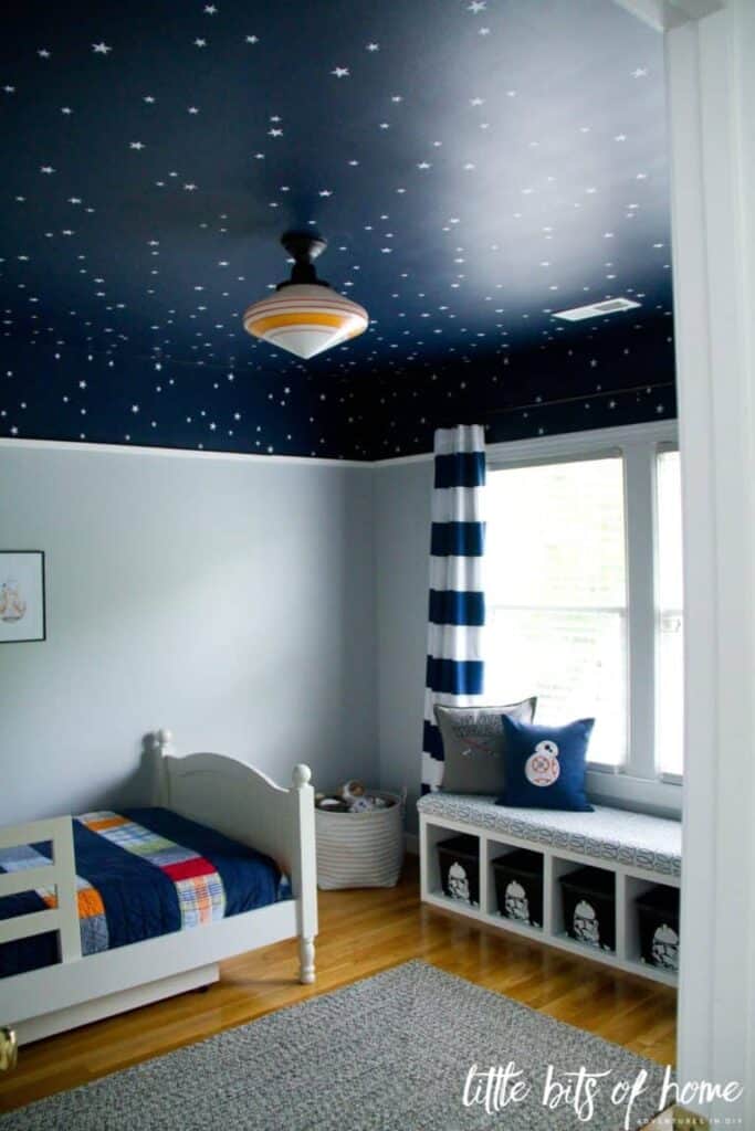 A boys room with Naval on the ceiling with white stars, blue and white striped curtains and light hardwood floors.
