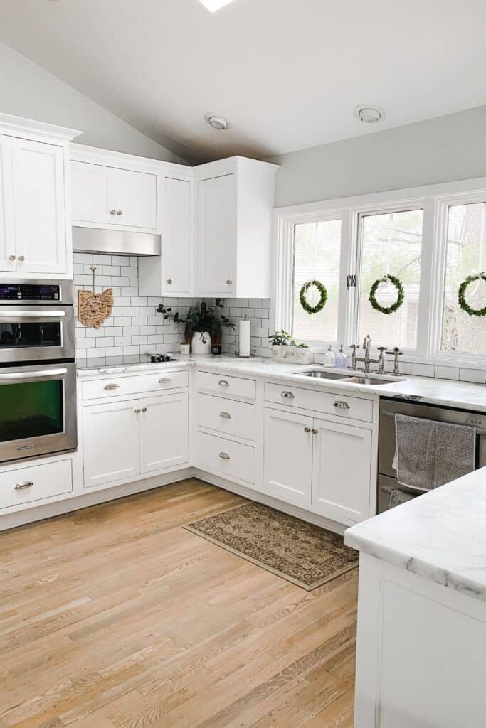 White cabinets in a kitchen with white counters and white subway tile backsplash with black grout.