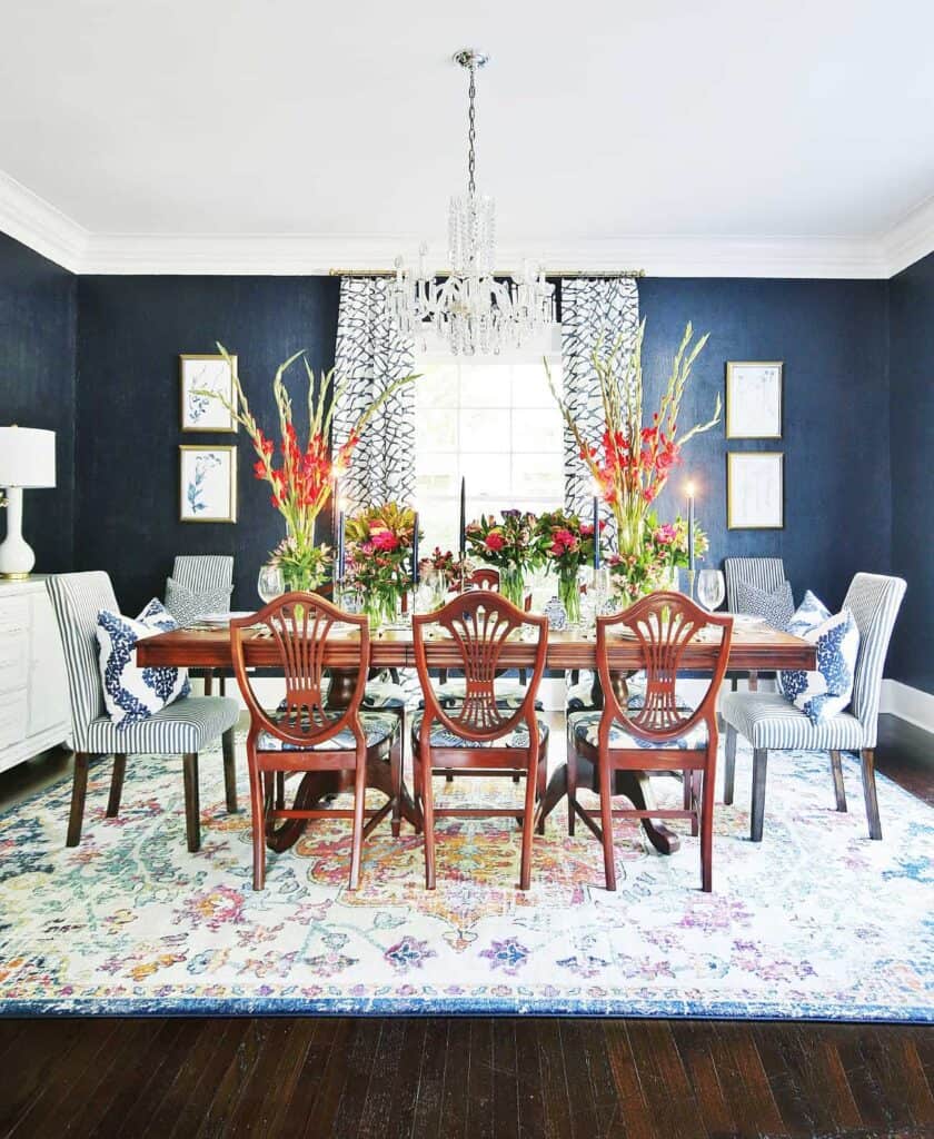 A dining room with Naval on the walls, a very colorful rug and a wood dining table with lots of flower arrangements on top.