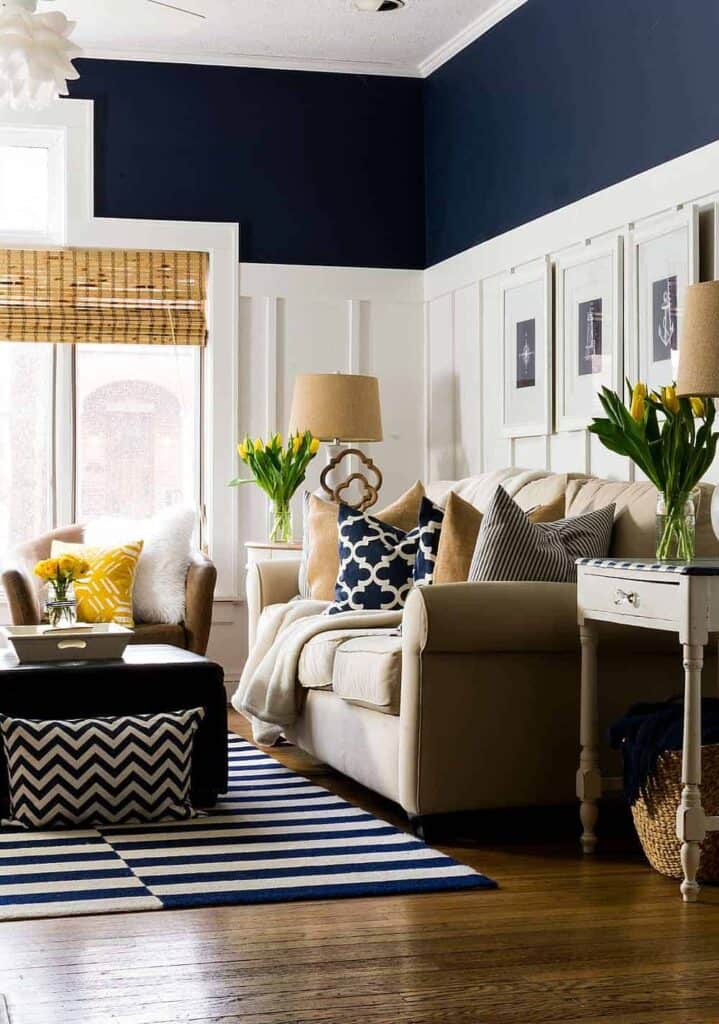A family room with board and batten painted white and Naval above, a beige couch, dark hardwood floors and yellow accents.