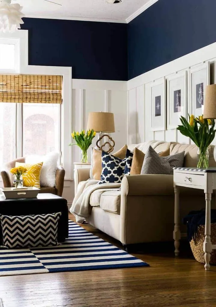 A family room with board and batten painted white and Naval above, a beige couch, dark hardwood floors and yellow accents.