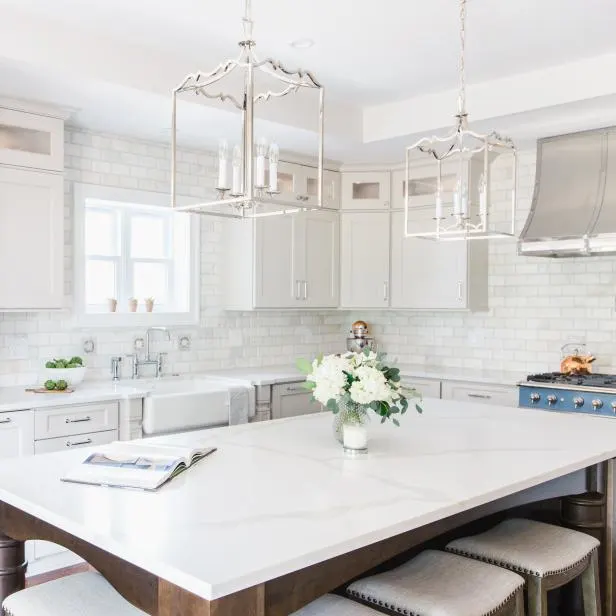 An island with a dark wood base and white countertops and the perimeter cabinets are white, marble subway tile backsplash and a pretty blue stove.
