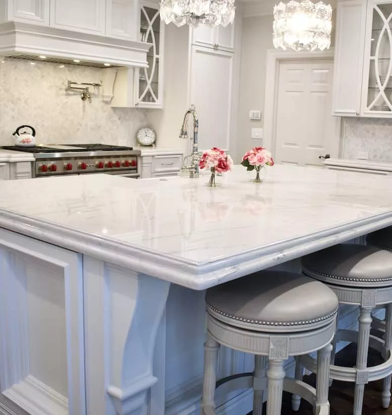 White cabinets with a white counter and two vases with pink and white flowers on top.