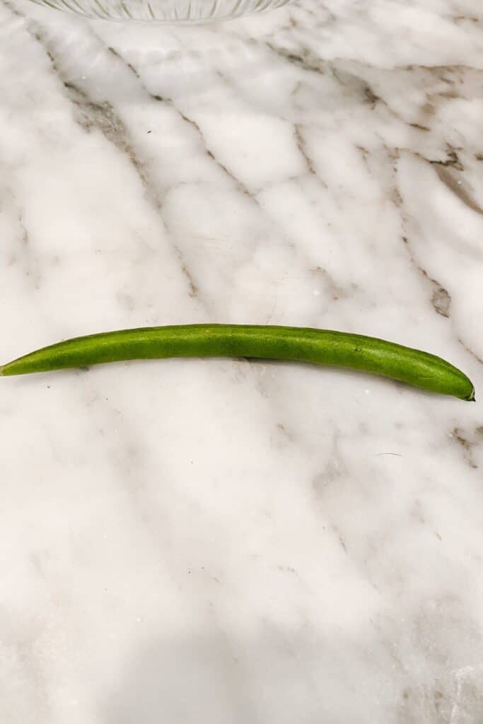 A green bean before being snapped sitting on my carerra countertop.