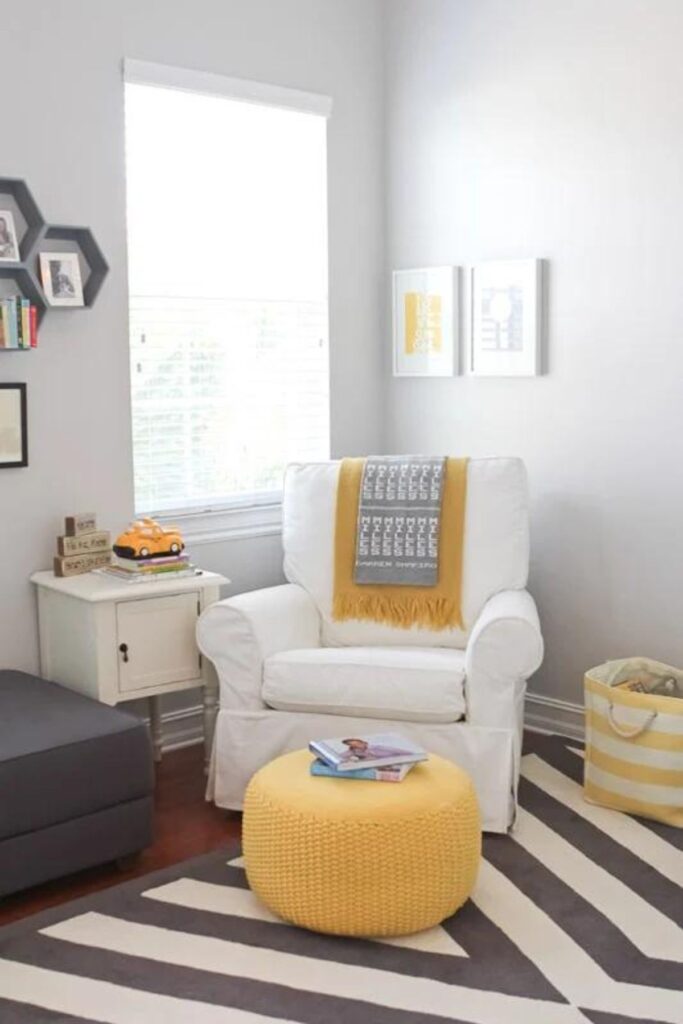 A nursery with On the Rocks on the walls, a white glider chair with a bright yellow poof and a gray and white striped rug.