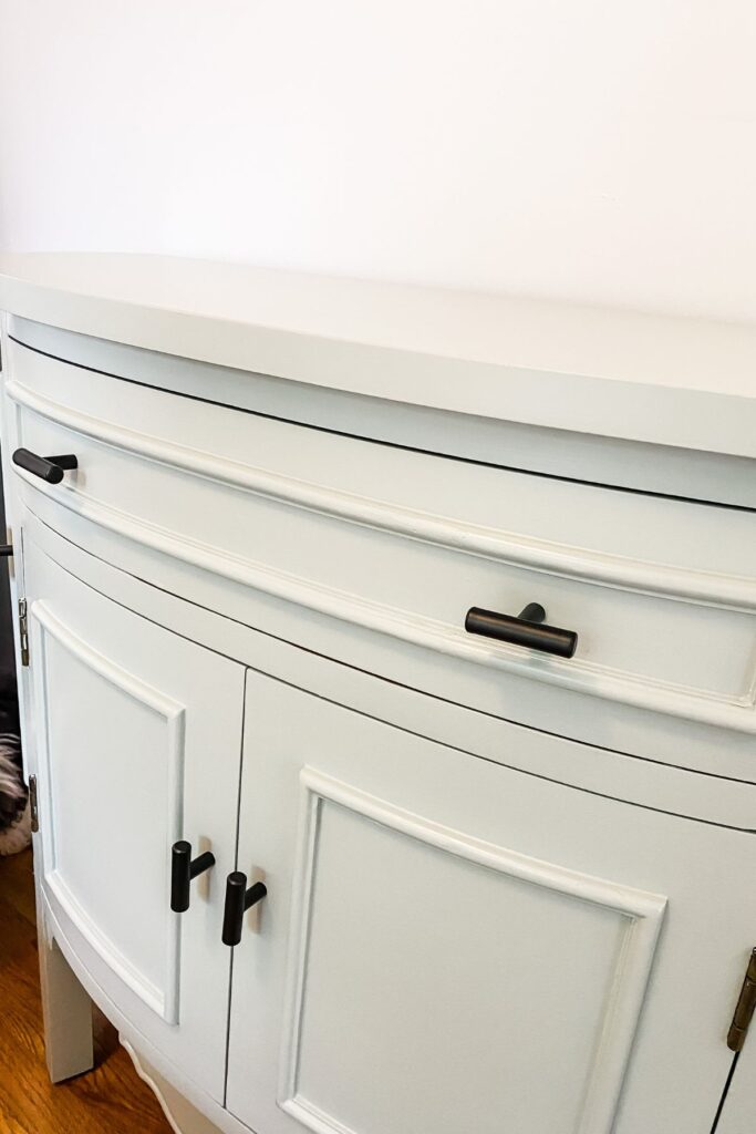 A finished cabinet painted sage green with black handles.