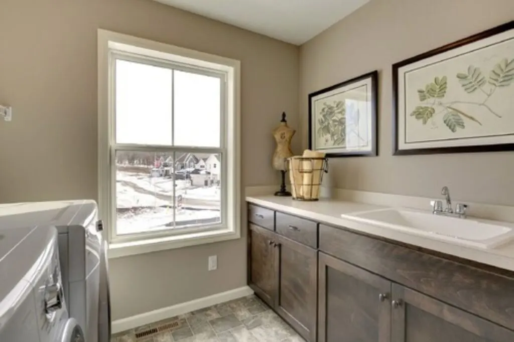 A laundry room with a large cabinet with sink and framed foliage prints on the walls.