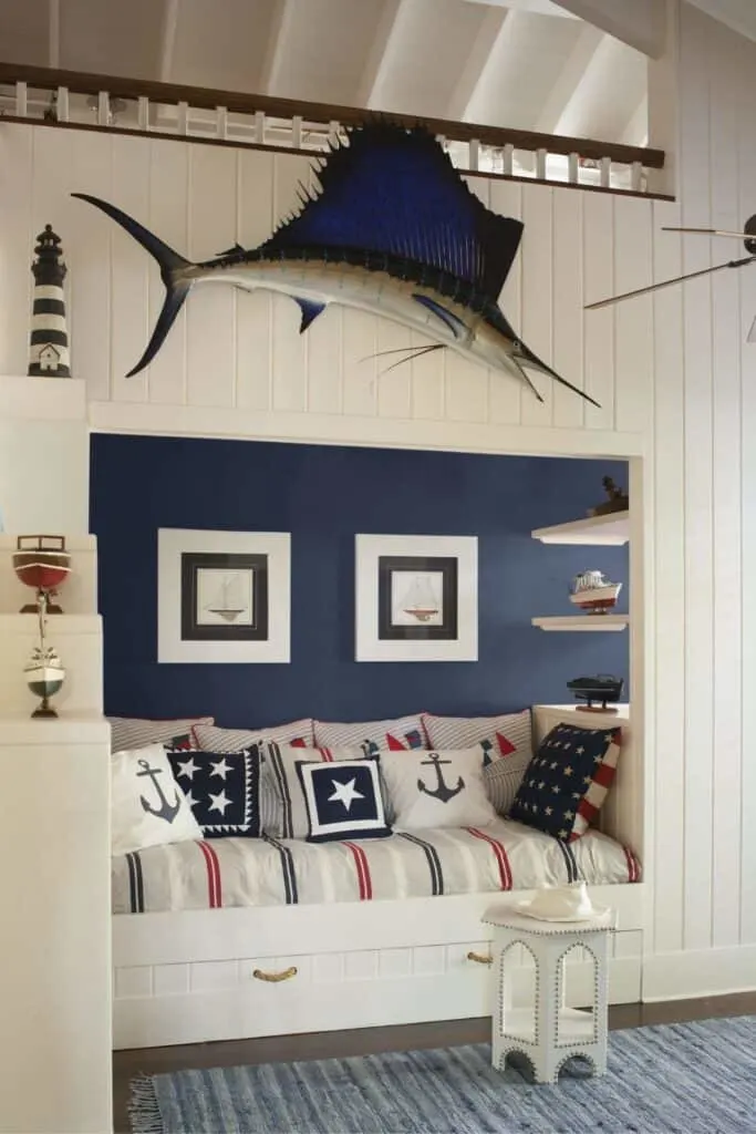 A nautical bedroom with an inset bed, white vertical shiplap and a blue accent wall with a swardfish hanging above the bed.