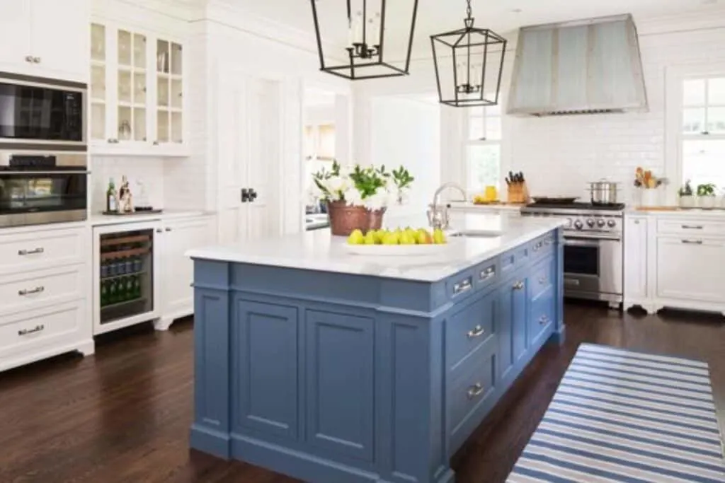 A kitchen with dark hardwood floors, white perimeter cabinets and a blue island in Van Deusen Blue.