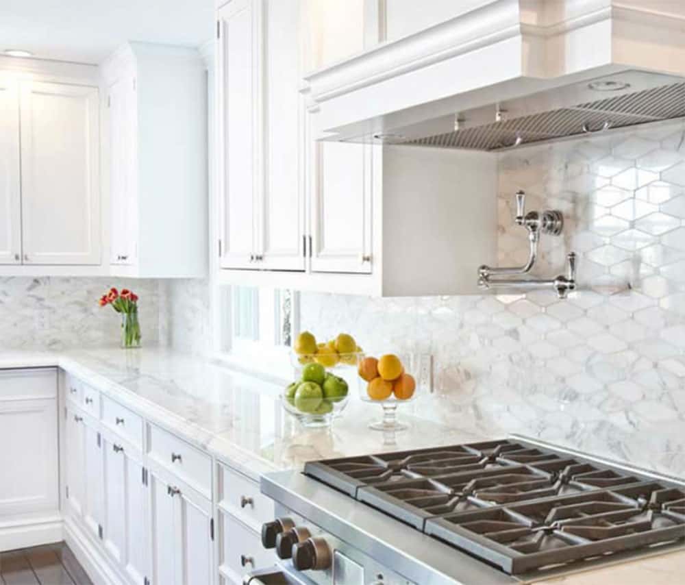 White cabinets, marble counters and a marble geometric backsplash with fruit displayed in clear dishes.