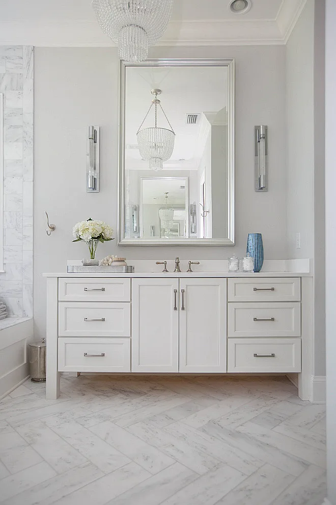 A bathroom with white cabinetry, marble tile on the shower walls and floors with silver hardware and mirror.
