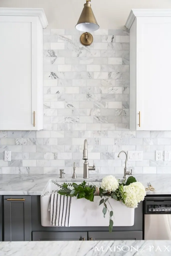white cabinets, marble backsplash in a staggered brick pattern with hydrangeas in the sink.