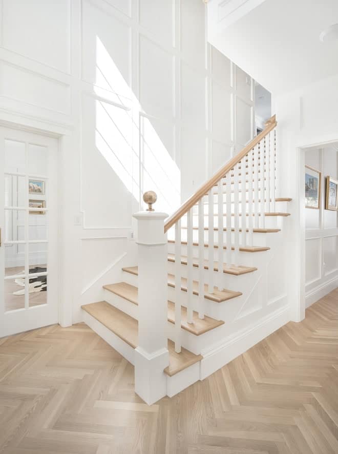 An entryway with a white staircase and light wood herringbone floors.