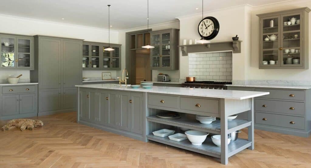 A kitchen with medium gray cabinets, white countertops and light herringbone wood floors.