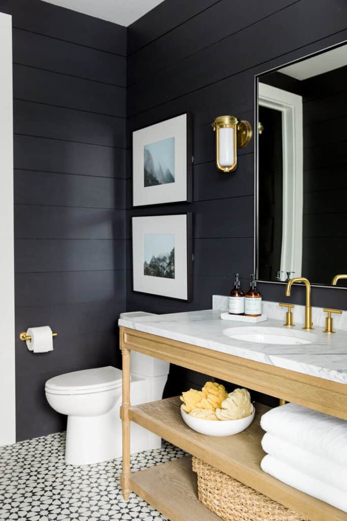 A bathroom with Soot painted shiplap, gold hardware, a white marble counter and a cabinet of light wood.