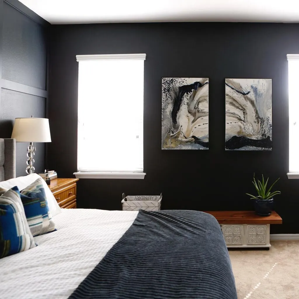 A bedroom with Soot on all the walls, white bedding and a dark wood bench with an aloe plant on it.