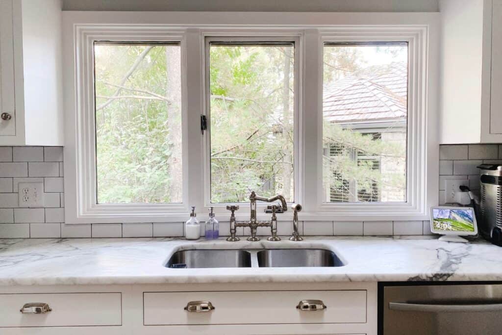 Kitchen sink with three windows over a silver faucet.