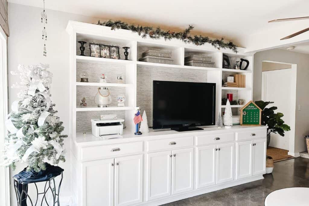 A view of the built-ins with garland on top and a flocked Christmas tree next to it.