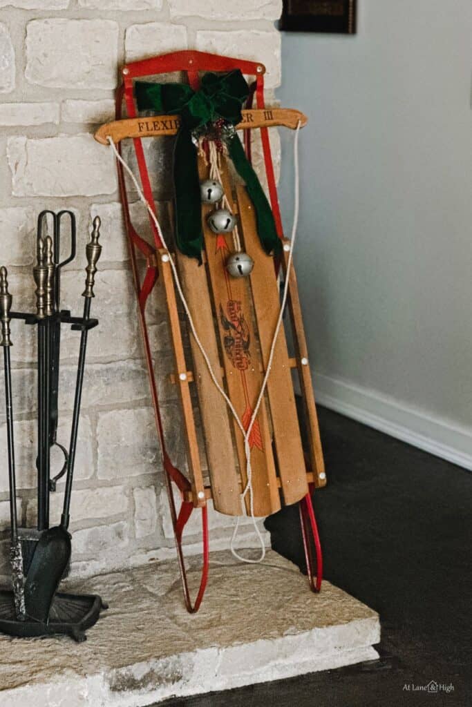 An antique sled with a green ribbon and bells hanging against my stone fireplace.