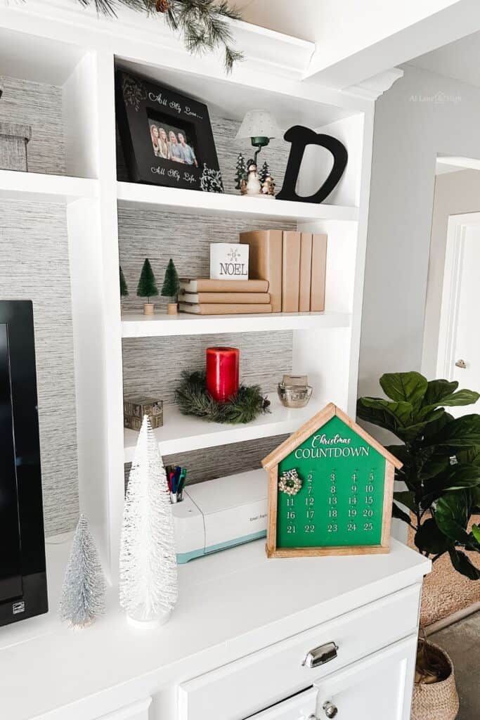 Accessories on the built-ins consisting of lots of different types of Christmas trees, an advent calendar and a red candle with greenery.