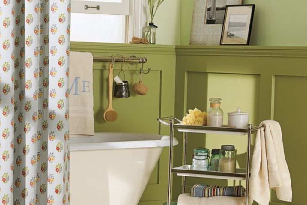 A bathroom with Hillside Green painted on board and batten with a claw foot tub and a bar cart with bath accessories.