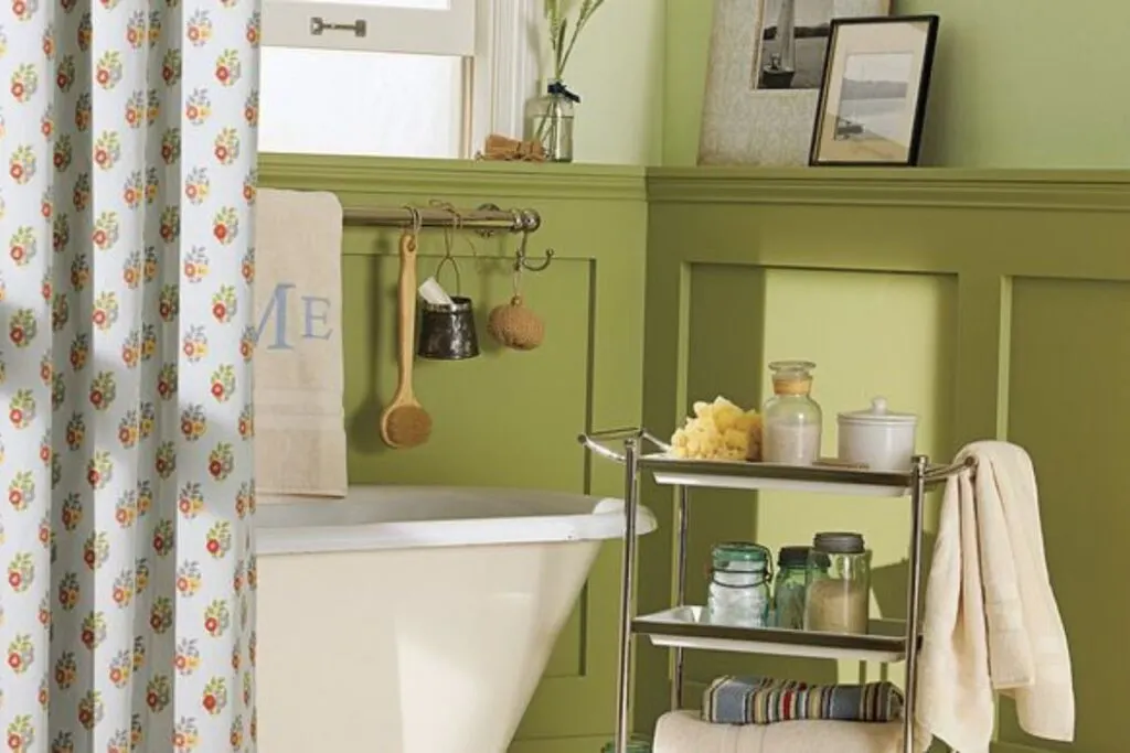 A bathroom with Hillside Green painted on board and batten with a claw foot tub and a bar cart with bath accessories.