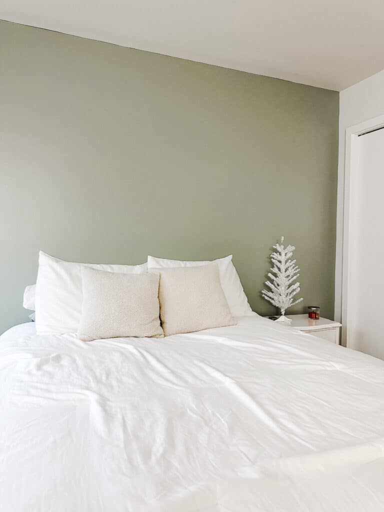 A bed with white bedding against a sage green headboard wall.
