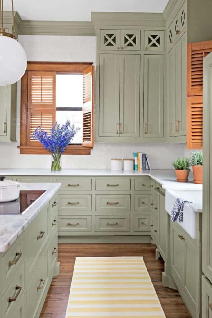 Clary Sage on kitchen cabinets with white counters and white subway tile backsplash and wood shutters on the windows.