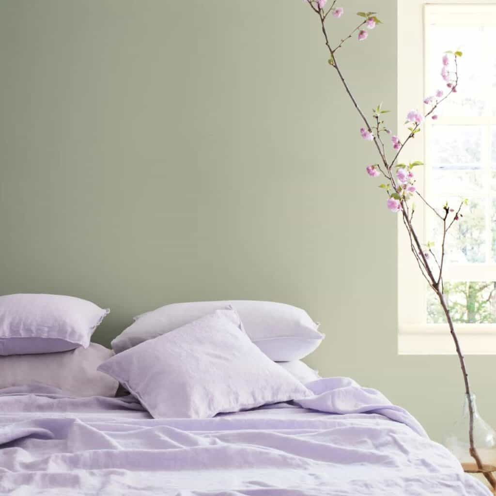 A bedroom with sage green on the walls and a tree branch with light pink flowers.