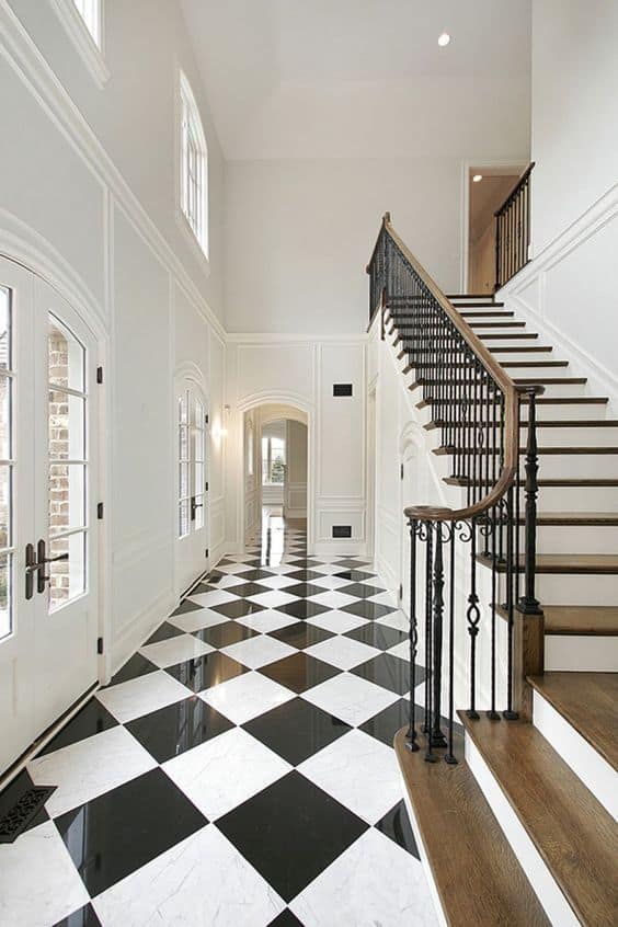 black and white checkered floor in an entry with a stairway with wood stairs and white walls with picture molding.