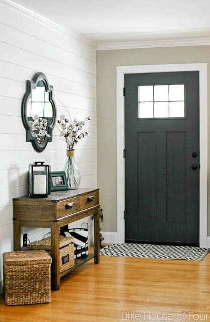 An entryway with white shiplap walls, Iron Ore on the inside of the front door and a wood console table and mirror above.