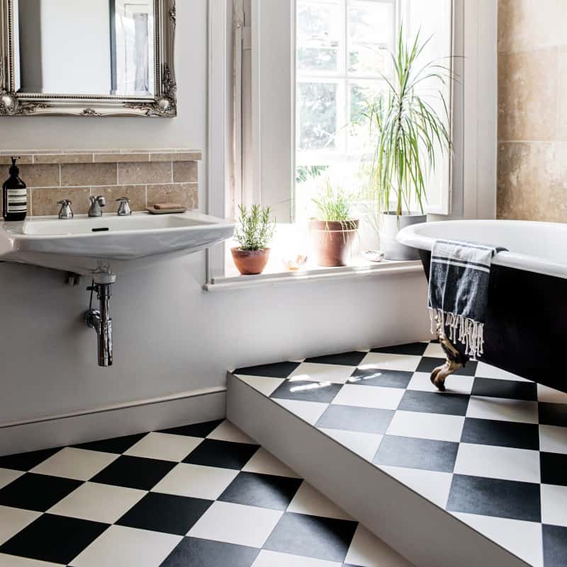 A bathroom with black and white checkered floor, a black and white claw foot tub and a pedestal sink.