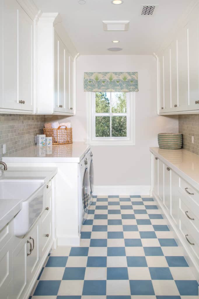 A laundry room with blue and white checkered tile, white cabinets and white countertops with a farmhouse sink.