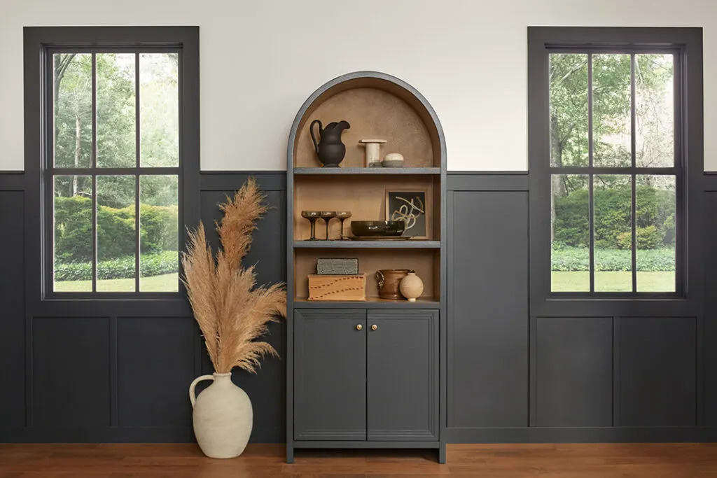 A dining room with board and batten and a cabinet in Iron Ore, white on the walls above and mid-toned hardwood floors.