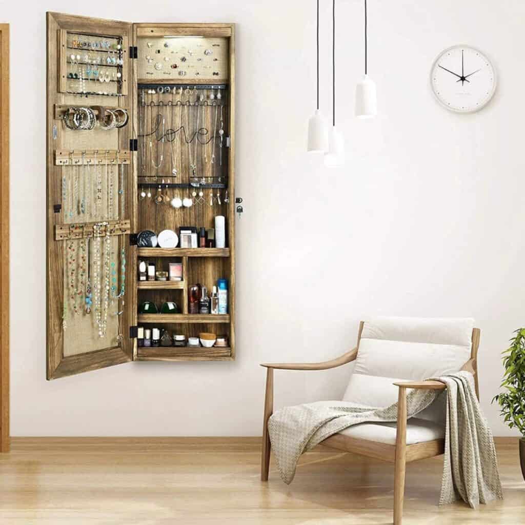 A wall mounted tall jewelry organizer with a door closure and a mirror on the front.