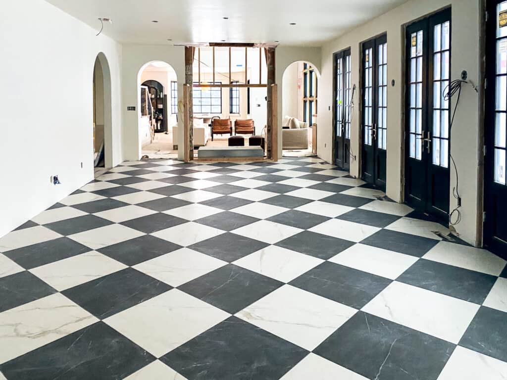 A large room with oversized black and white checkered tile, black french doors on one side of the room and arched doorways at the far end.