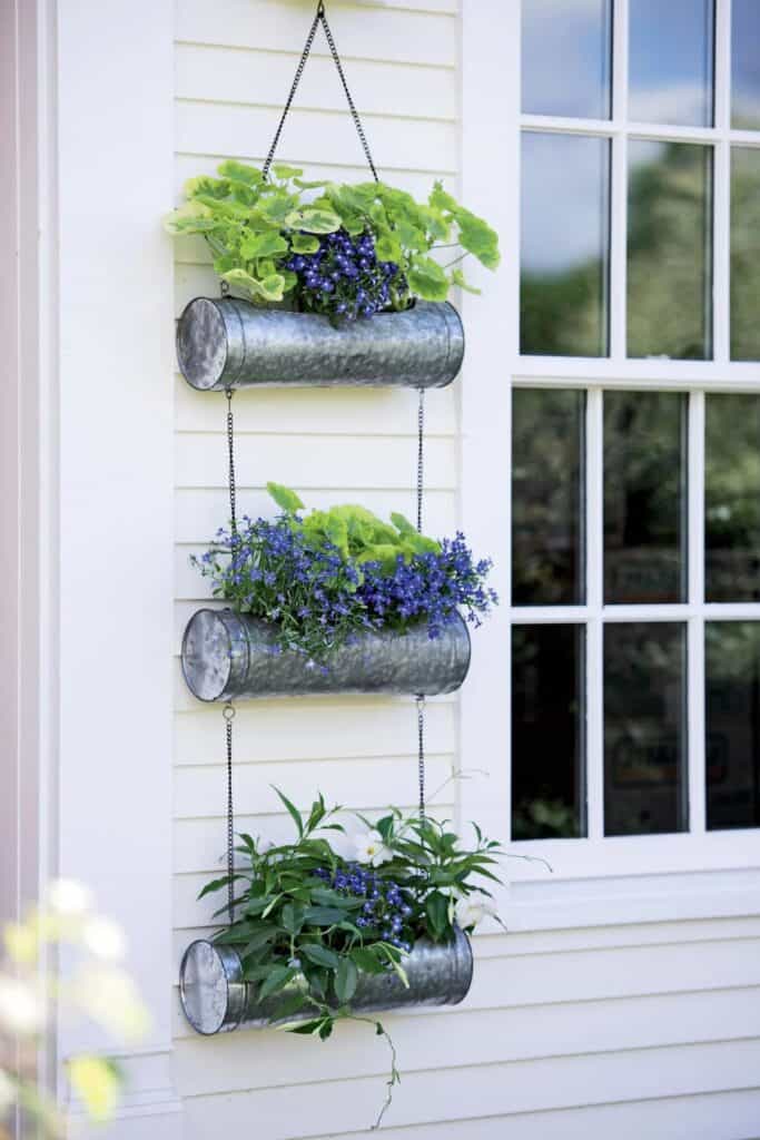 Hanging galvanized circular planters that hang on the wall with blue and green flowers in them.