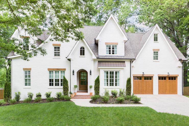 The exterior of a large Tudor style home painted with Aesthetic White, wood garage doors and black accents.