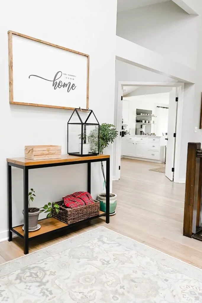 A wood and black metal console table with plants, a wood box and a basket on it.