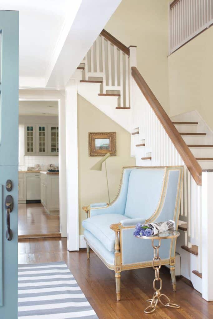 Pashmina on the walls in an entryway with a white staircase and a blue setee.