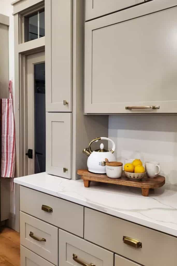 Pashmina on kitchen cabinets with gold hardware, a marble counter, white backsplash.