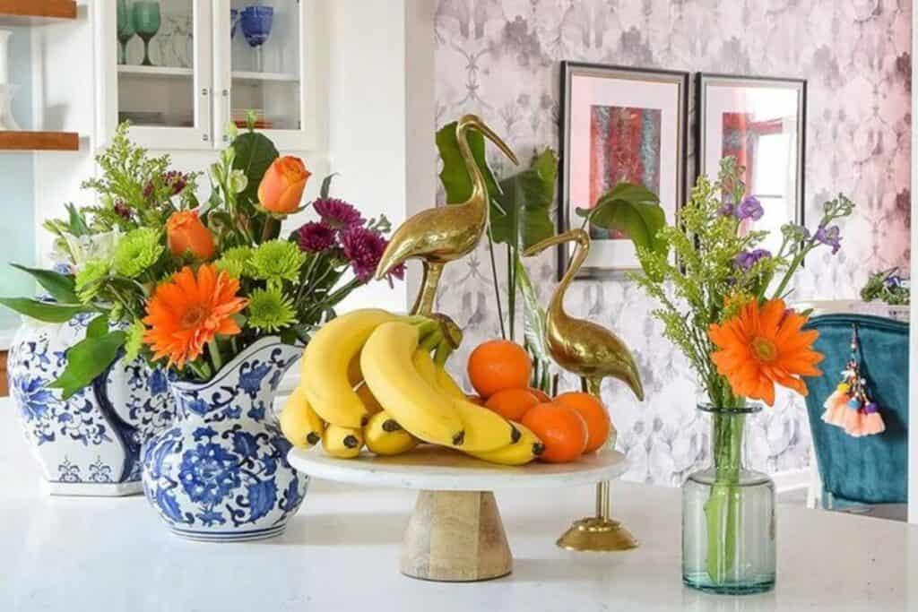 A colorful kitchen with fruit on a cake plate and a blue and white pitcher with colorful flowers.