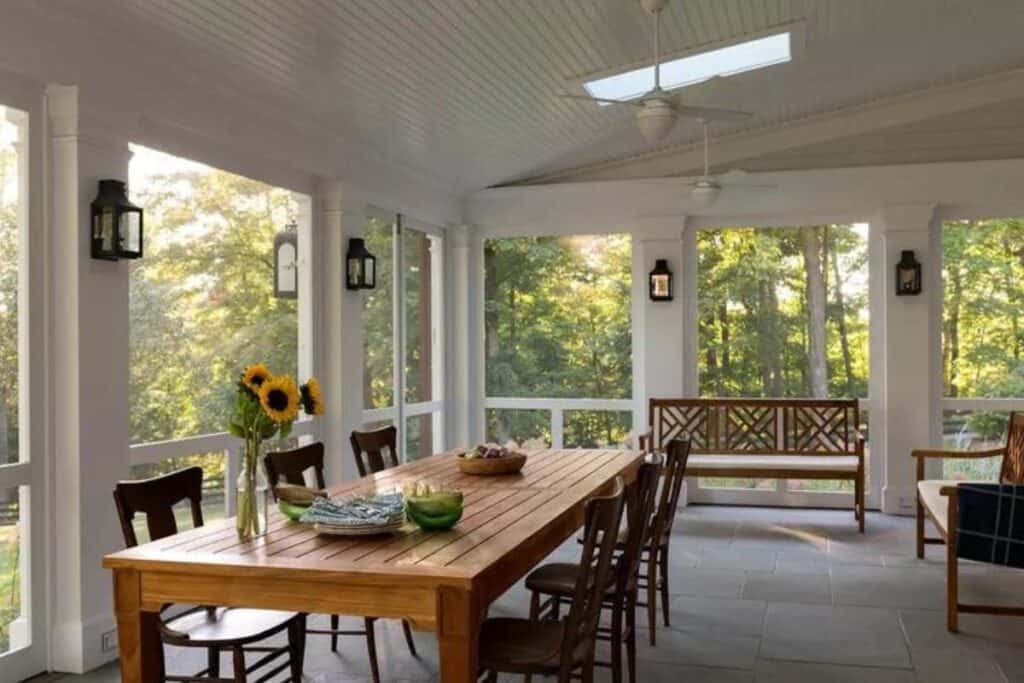 A screened in porch with a wood dining table and chairs and two wood benches.