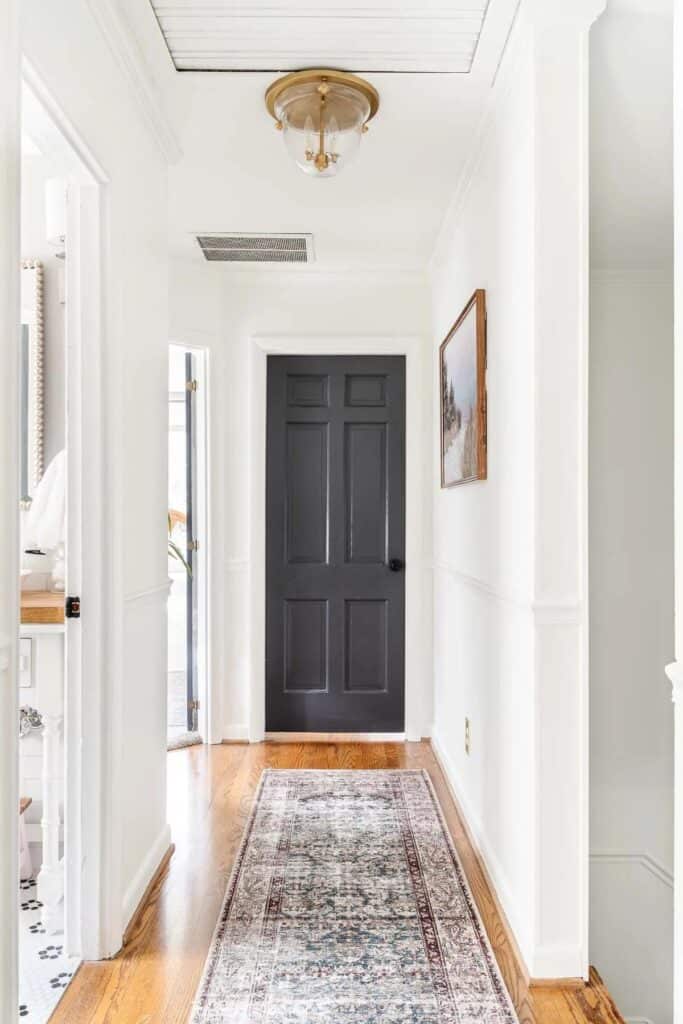 A black interior door at the end of a hallway with light wood floors and white walls.